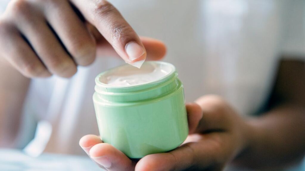 How to Take Care of Your Nails Naturally at Home in 2025 12 a woman dipping her finger in a tub of moisturiser that she is going to use to make her nails grow faster